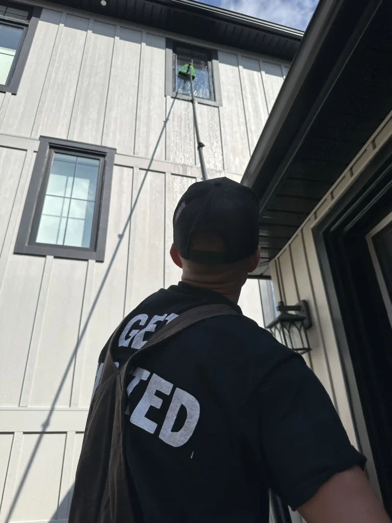 Gutter Ghosts technician washing second-story window with telescopic water-fed pole