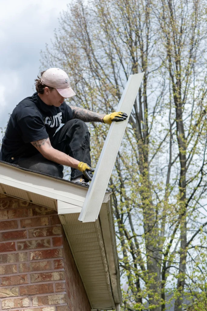 josh-chapman-placing-a-gutter-gaurd Gutter Ghosts technician installing perforated aluminum gutter guard on two-story brick home