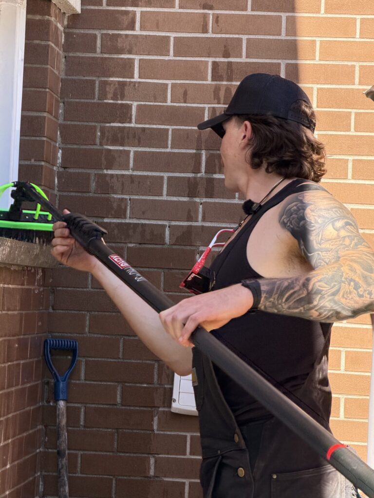 cleaning-window-brick-ledger-markham Josh Chapman cleaning using water-fed pole with green brush to wash lower window on brick house exterior during residential window cleaning service in Pickering